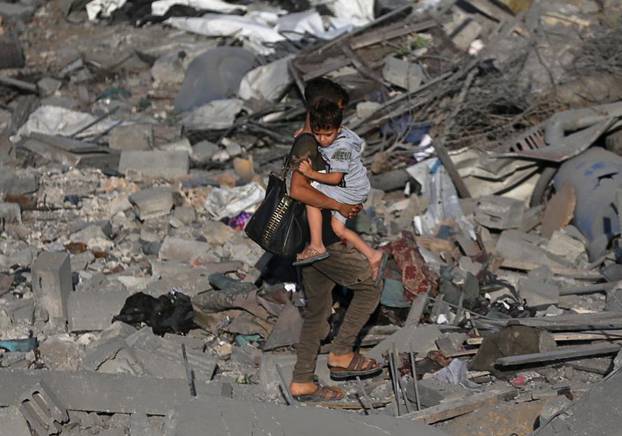 Palestinian boy carries his brother as he walks through the debris of a house destroyed in an Israeli air strike in the southern Gaza Strip