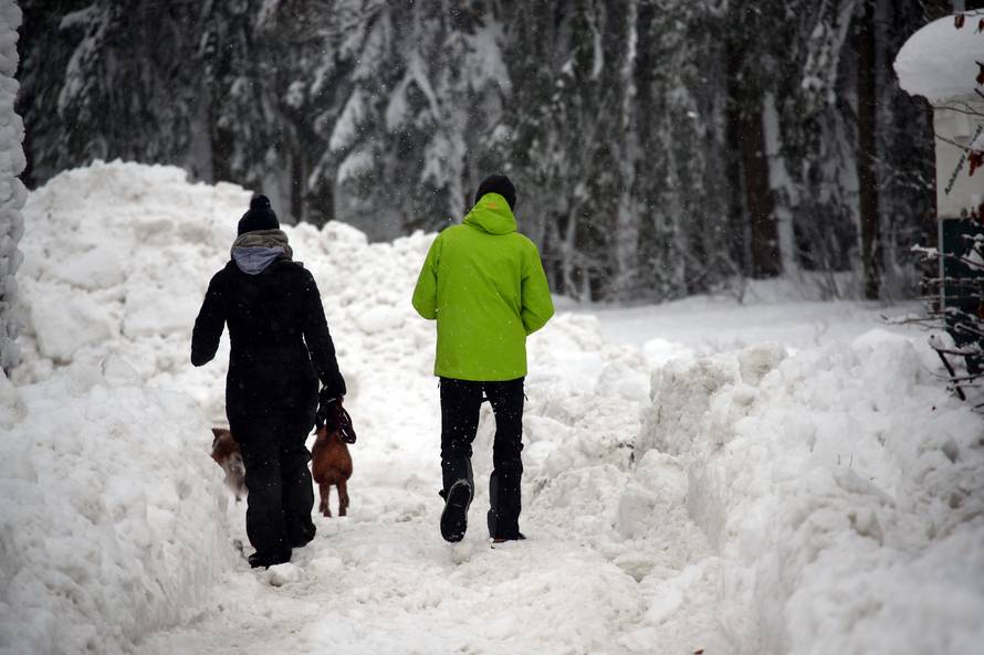 A couple walks their dogs on an icy road after heavy snowfall near Reitham