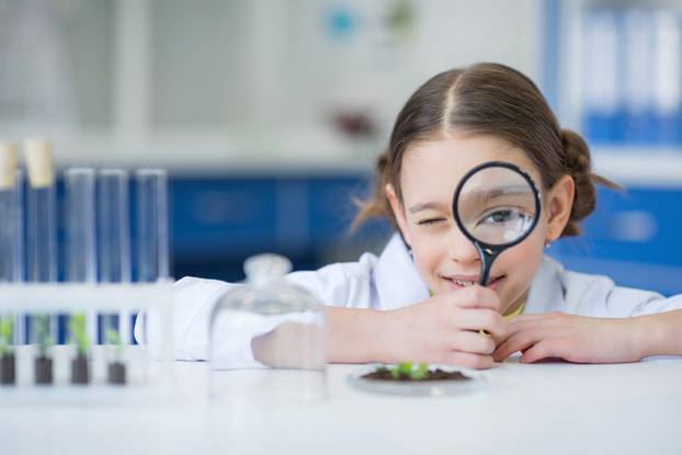 girl scientist holding magnifying glass and looking at camera