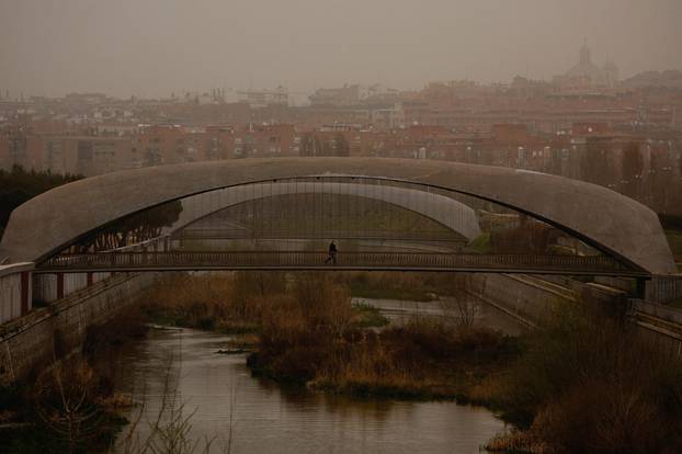 A person wearing a face mask crosses a bridge as storm Celia blew sand from the Sahara desert over Madrid