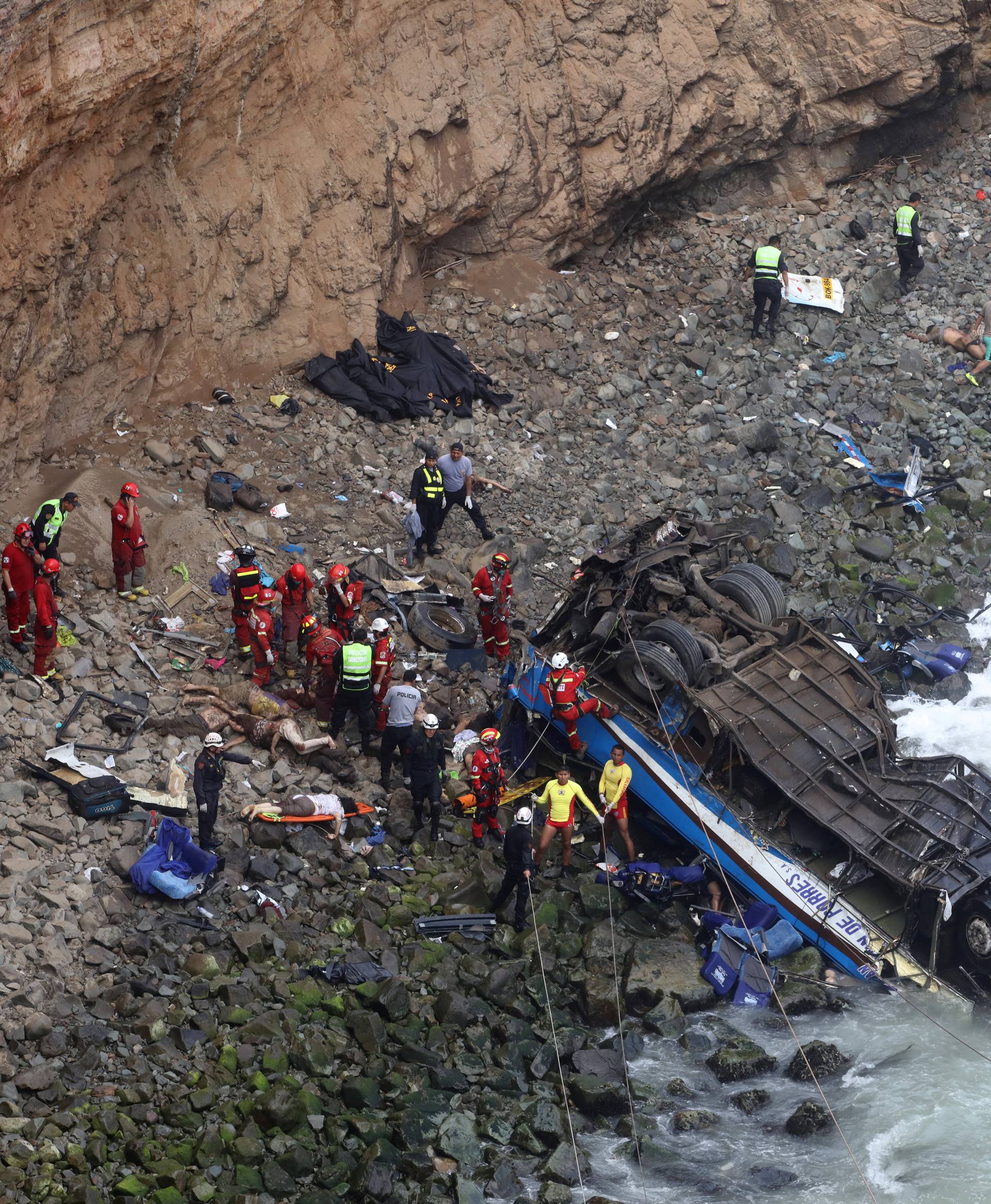 Rescue workers work at the scene after a bus crashed with a truck and careened off a cliff along a sharply curving highway north of Lima