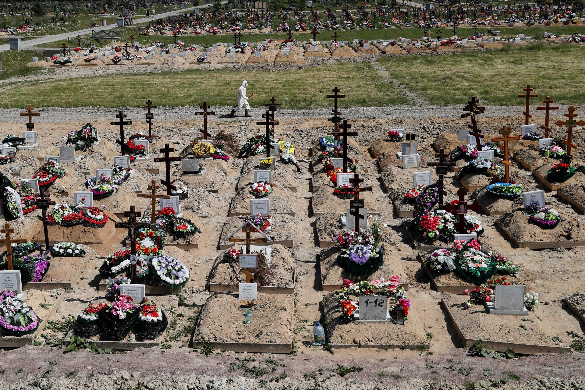 A grave digger wearing personal protective equipment walks along a graveyard on the outskirts of Saint Petersburg