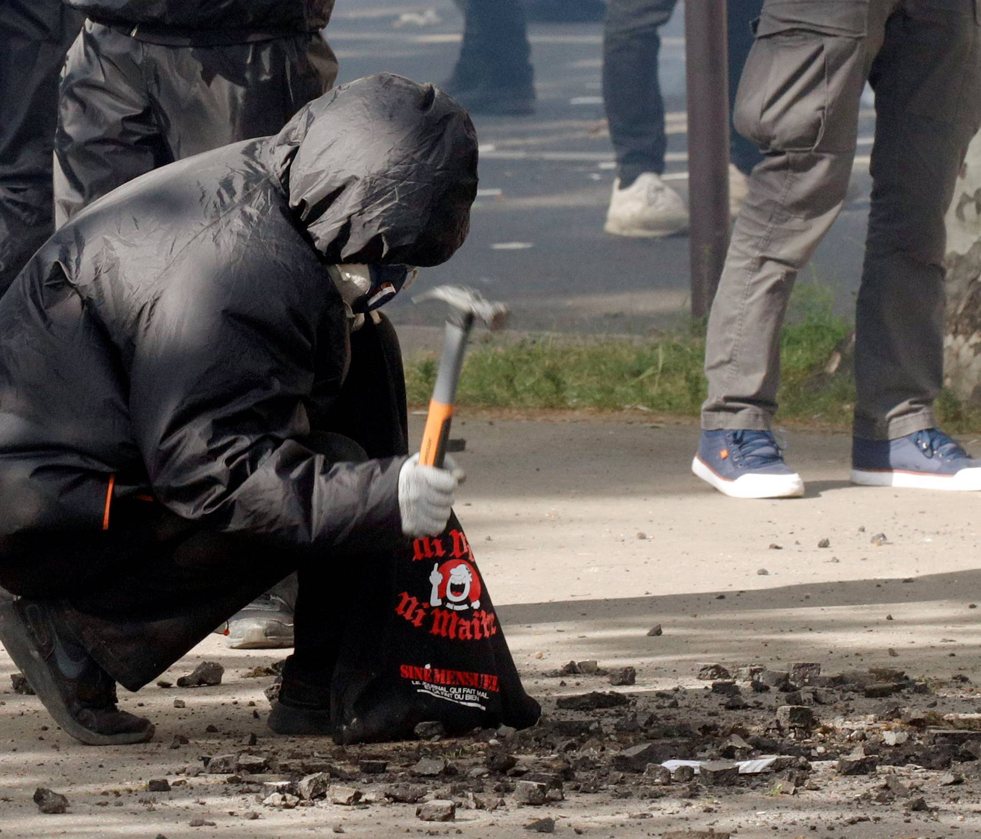 A masked and hooded protester uses a hammer to gather rocks during clashes with French CRS riot police at the May Day labour union rally in Paris