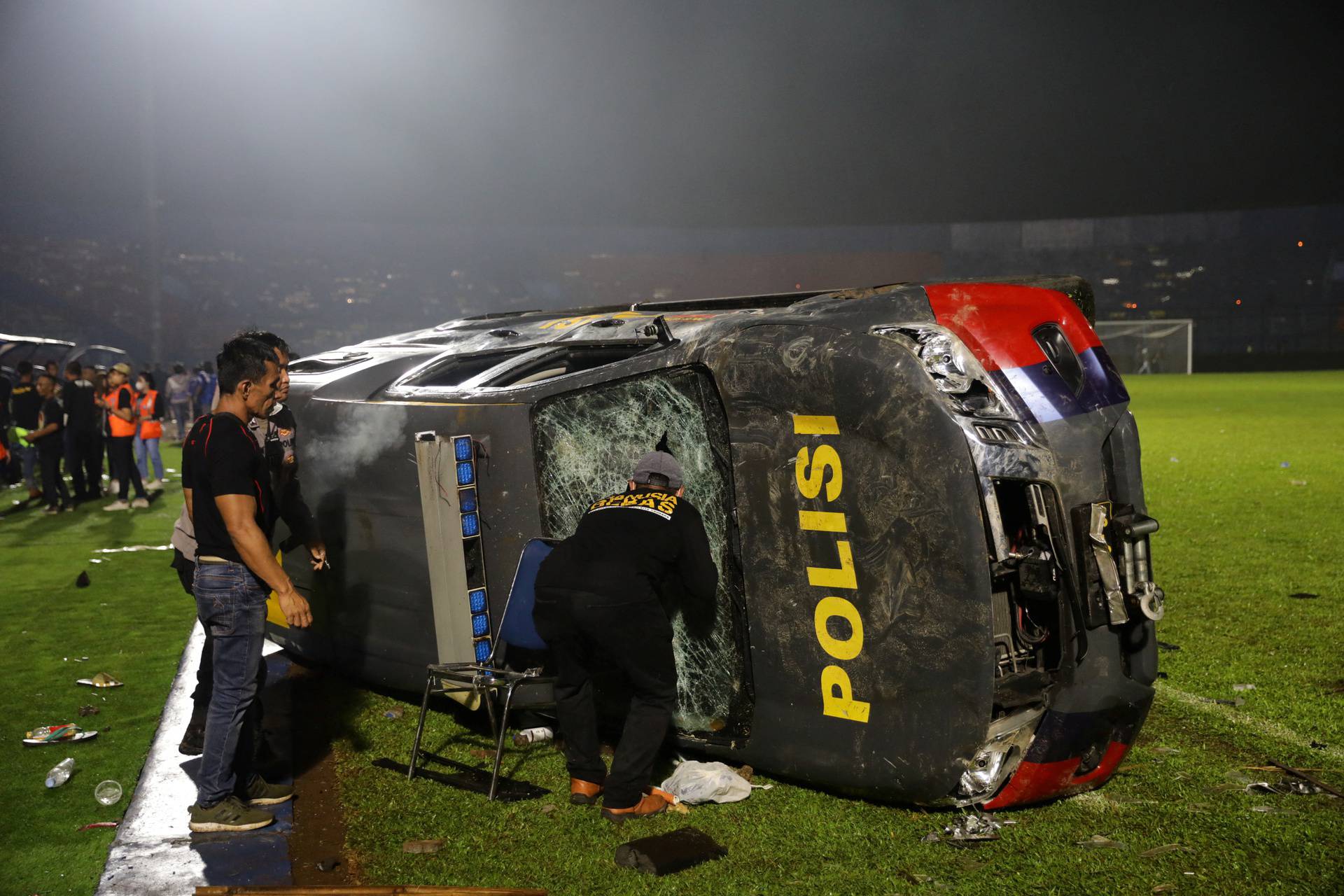 People stand next to a damaged car following a riot after the league BRI Liga 1 football match between Arema vs Persebaya at Kanjuruhan Stadium