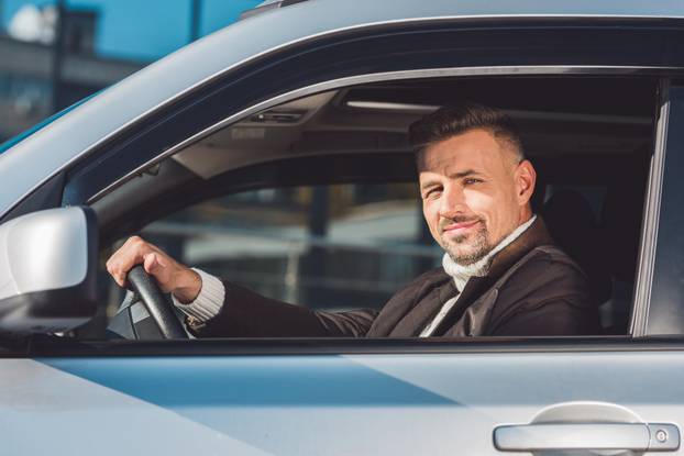 Handsome man holding steer and sitting in car 