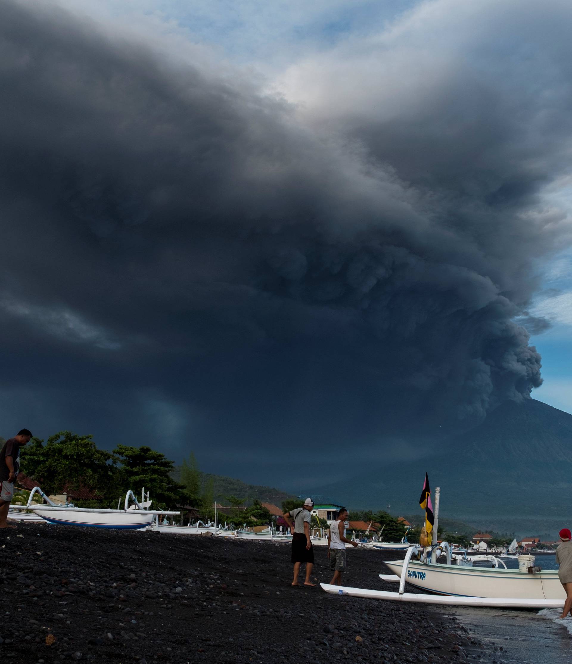 Indonesia's Mount Agung volcano erupts as fishermen pull a boat onto the beach in Amed, Bali