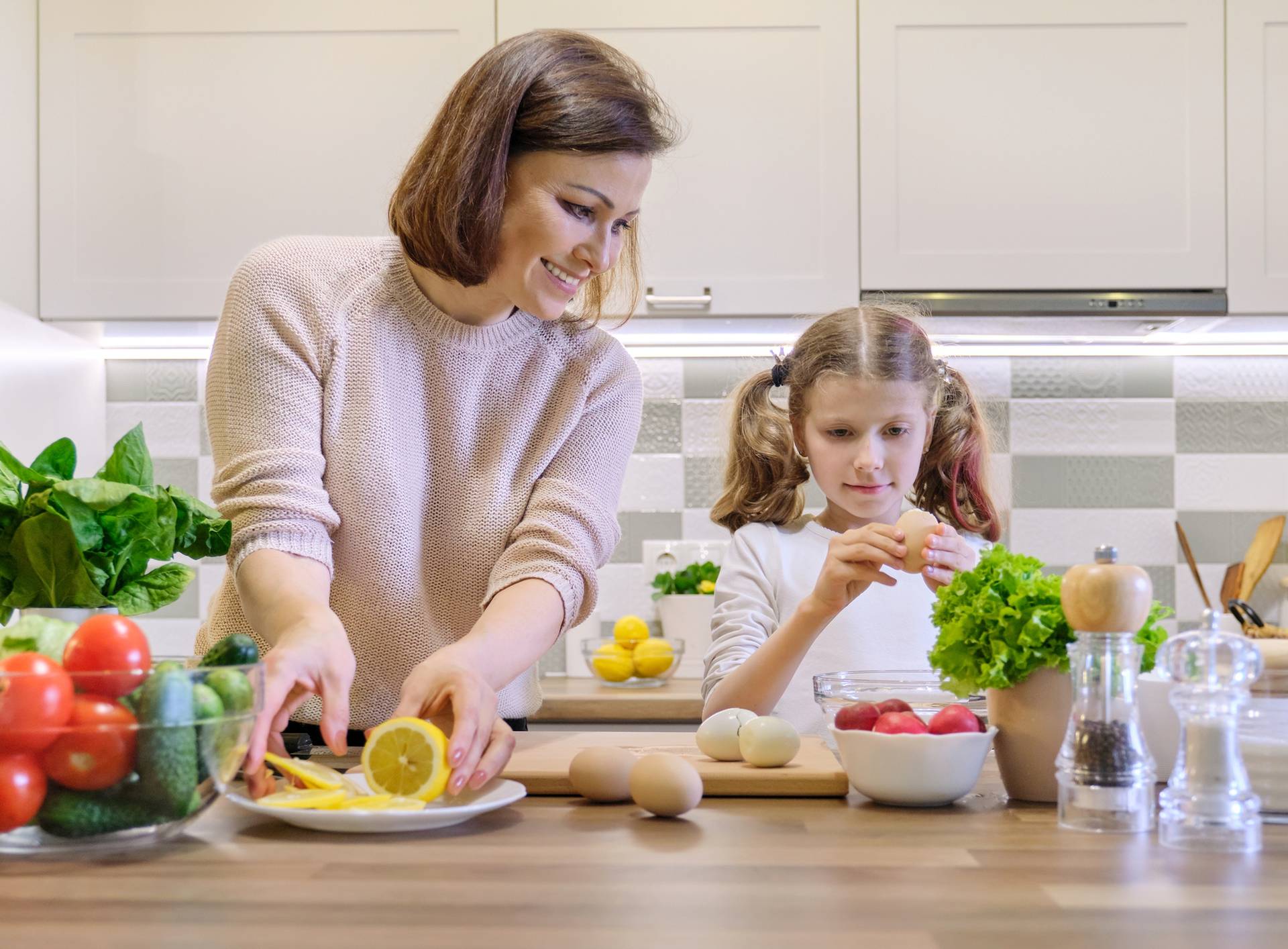 Smiling mother and daughter 8, 9 years old cooking together in kitchen vegetable salad. Healthy home food, communication parent and child.