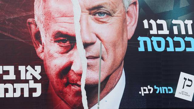 FILE PHOTO: A boy looks up at a Blue and White party election campaign banner depicting its leader, Israeli Defence Minister Benny Gantz, alongside Israeli Prime Minister Benjamin Netanyahu, ahead of the March 23 ballot, in Bnei Brak