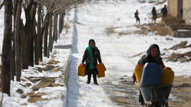 An Afghan girl carries empty water containers on a snow-covered street in Kabul
