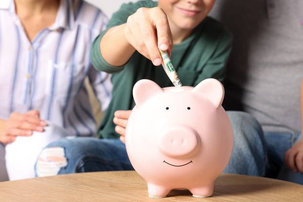 Boy with his mother putting money into piggy bank at home, close