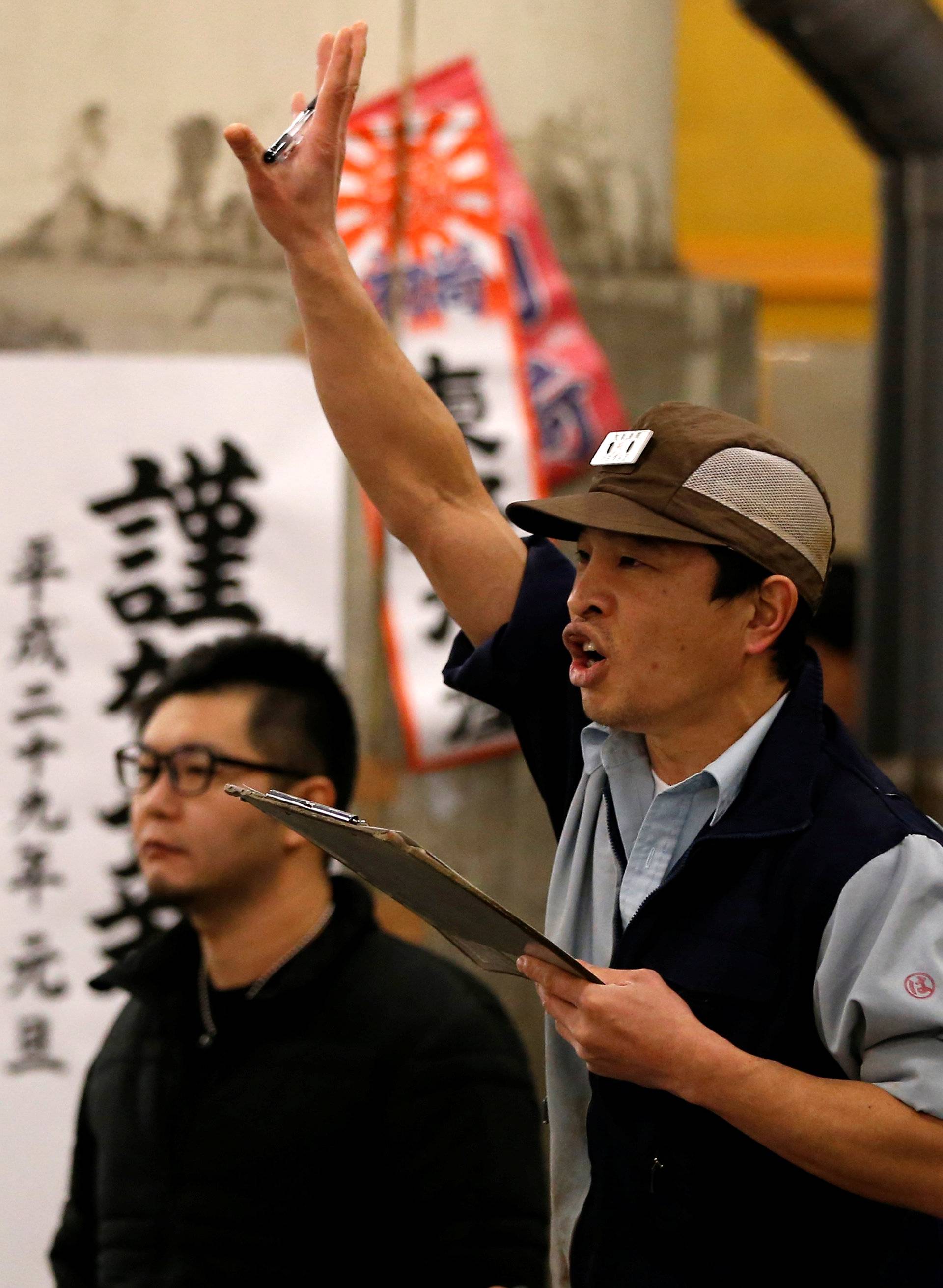 An auctioneer raises his hand as he starts the New Year's auction of the frozen tuna while wholesalers check the quality of frozen tuna displayed at the Tsukiji fish market in Tokyo, Japan