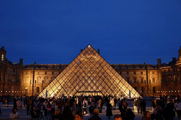 People walk near the glass Pyramid of the Louvre museum 
