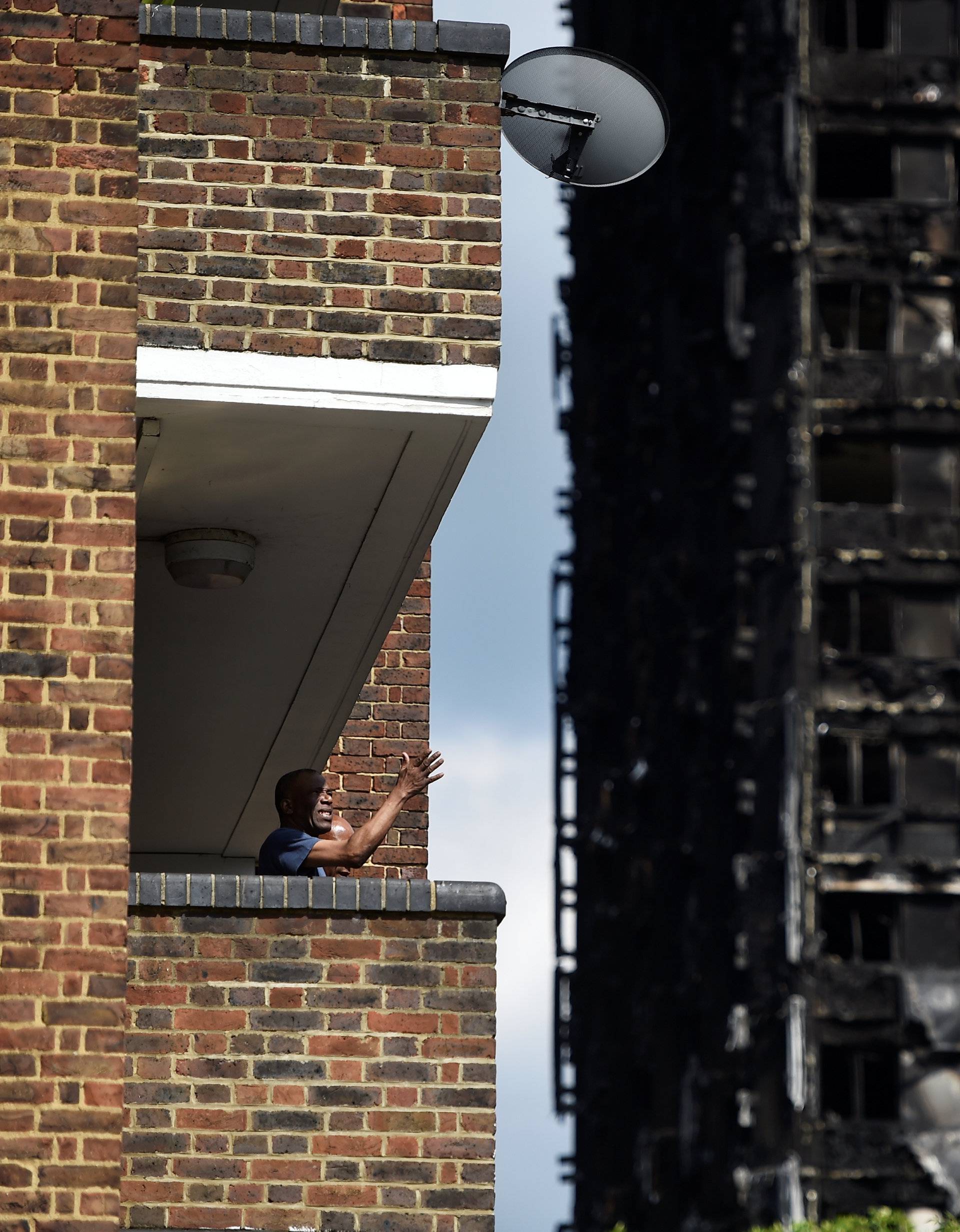 A man stands on his balcony in front of the burnt out shell of the Grenfell apartment tower block in North Kensington, London