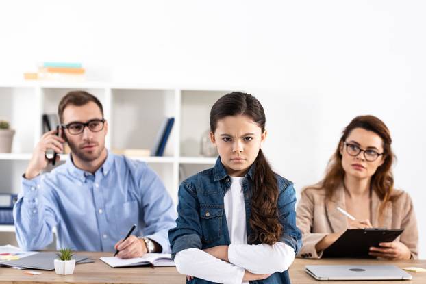 selective focus of sad kid with crossed arms near parents in office 