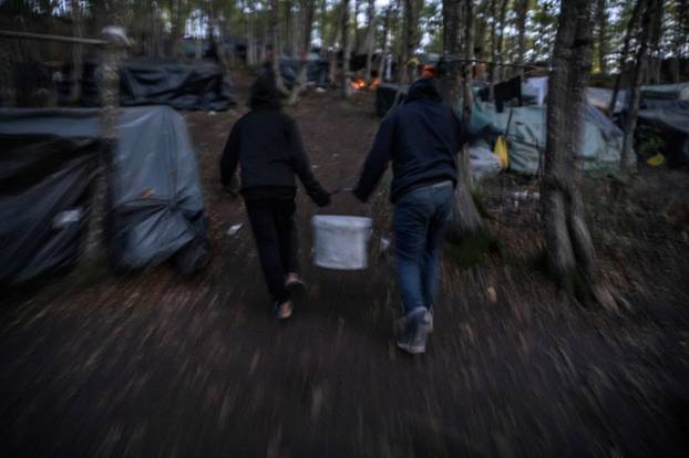 Migrants from Bangladesh carry a basket of water in the woods near Velika Kladusa