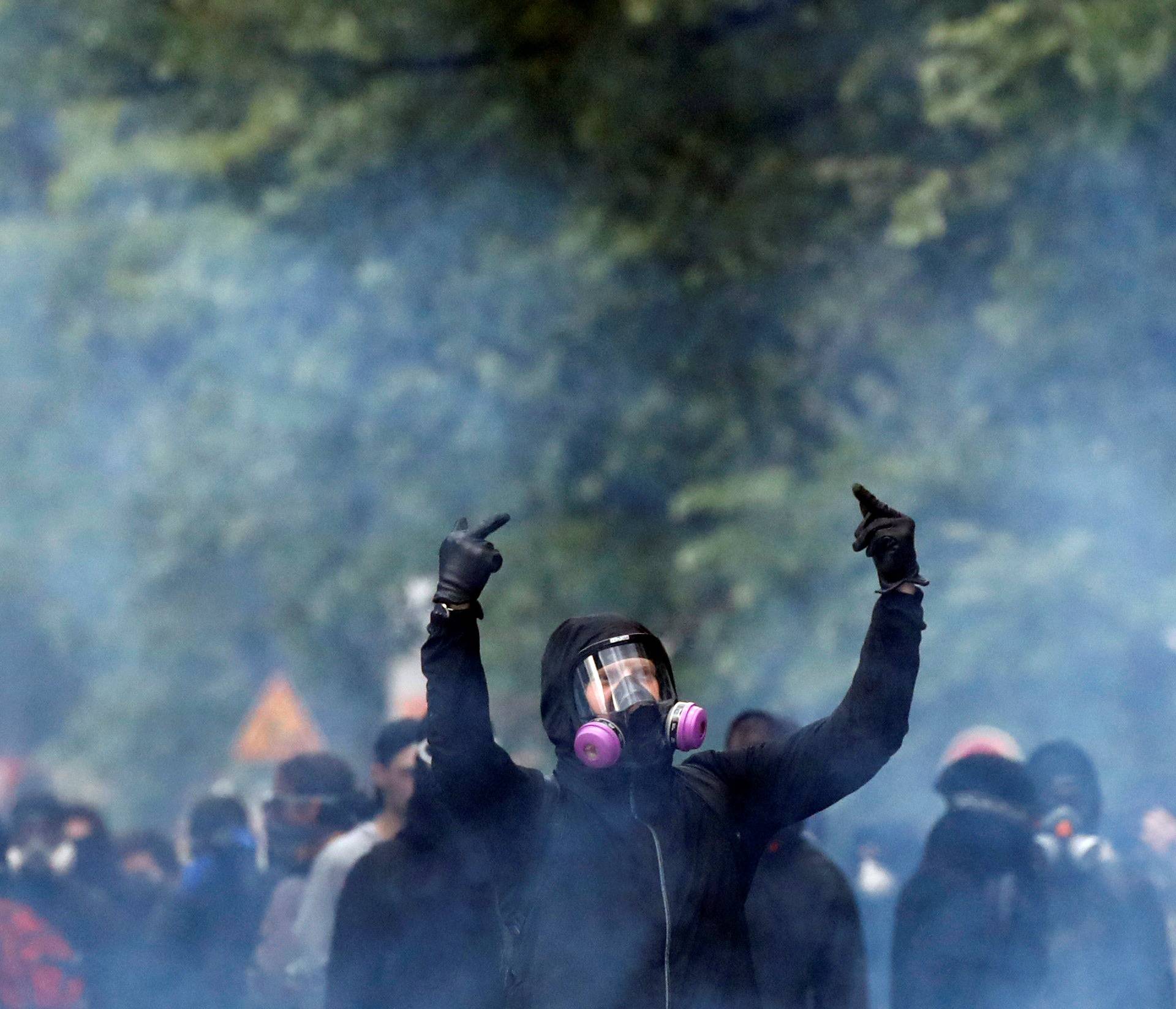 Tear gas floats in the air as a masked protester reacts during clashes with French riot police at the May Day labour union rally in Paris