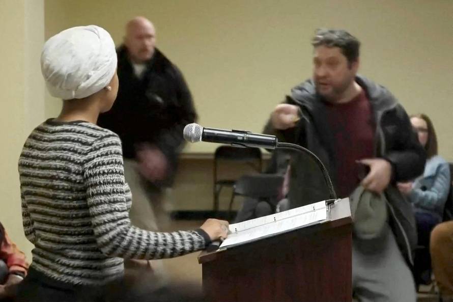 A man shouts at U.S. Rep. Ilhan Omar after spraying her, during a town hall meeting in Minneapolis