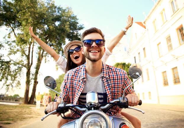 Portrait of happy young couple on scooter enjoying road trip