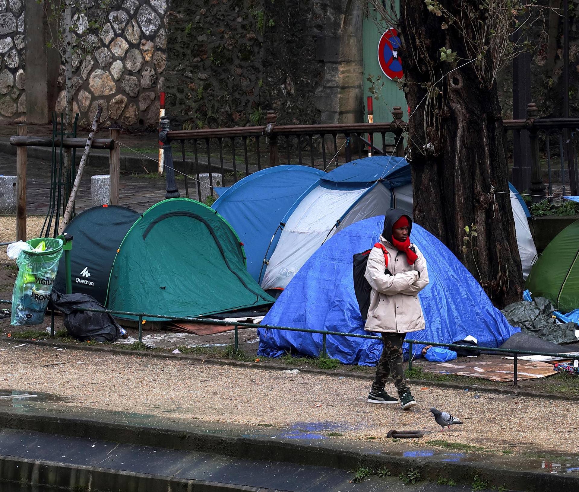 FILE PHOTO: A migrant walks next to a row of tents installed on the banks of Canal Saint-Martin in Paris