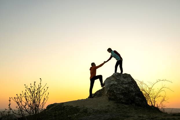 Man and woman hikers helping each other to climb a big stone at 