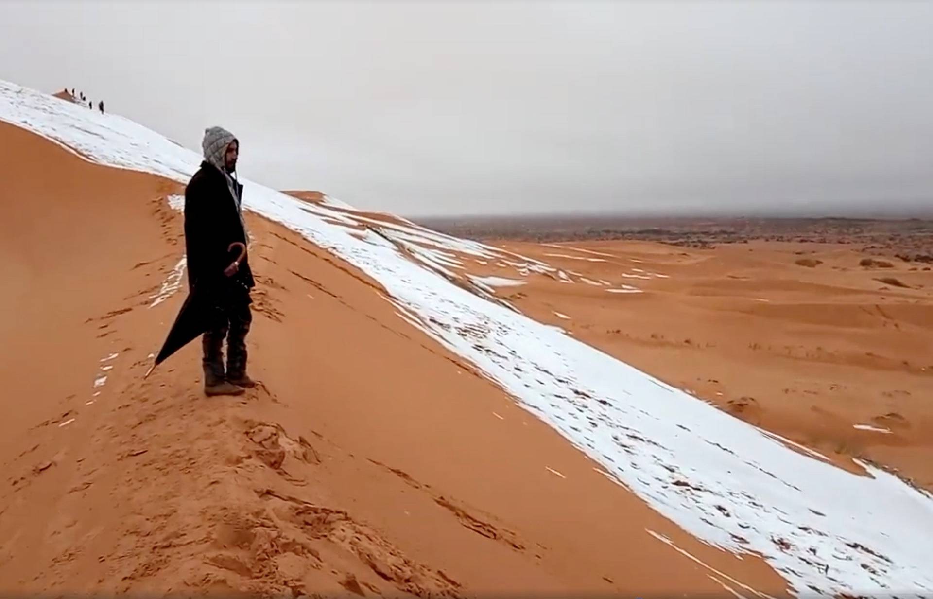 A man looks at at a snow-covered slope in the Sahara, Ain Sefra