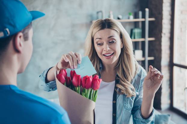 Close-up portrait of nice attractive lovely pretty cheerful cheery wavy-haired girl getting receiving congrats card birthday greetings red flowers at modern industrial loft brick style interior room