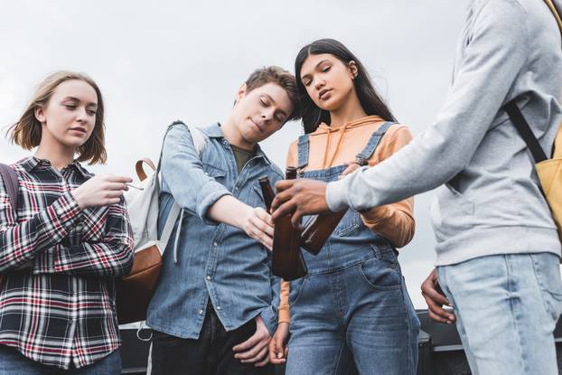 teenagers clinking with glass bottles and smoking cigarette on roof 