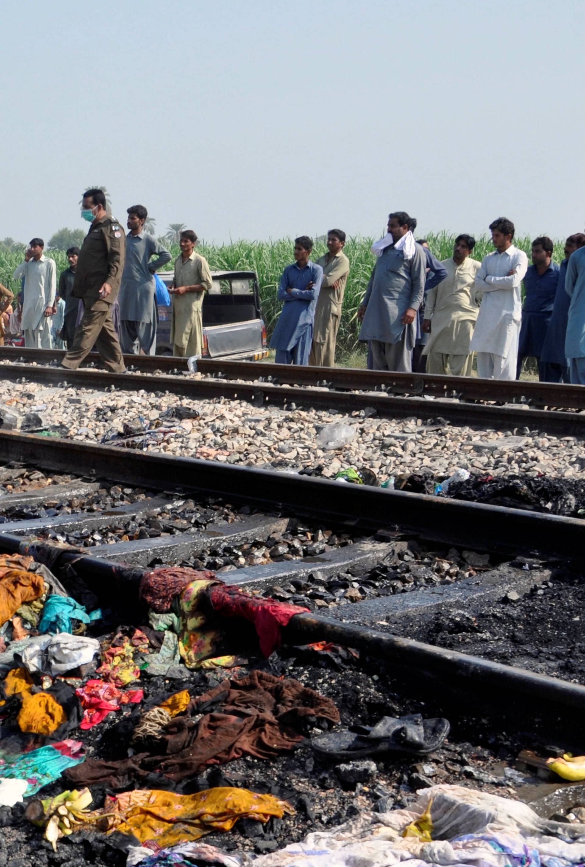 People gather near a track with the charred belongings of passenger victims, after a fire broke out in a passenger train and destroyed three carriages near the town of Rahim Yar Khan