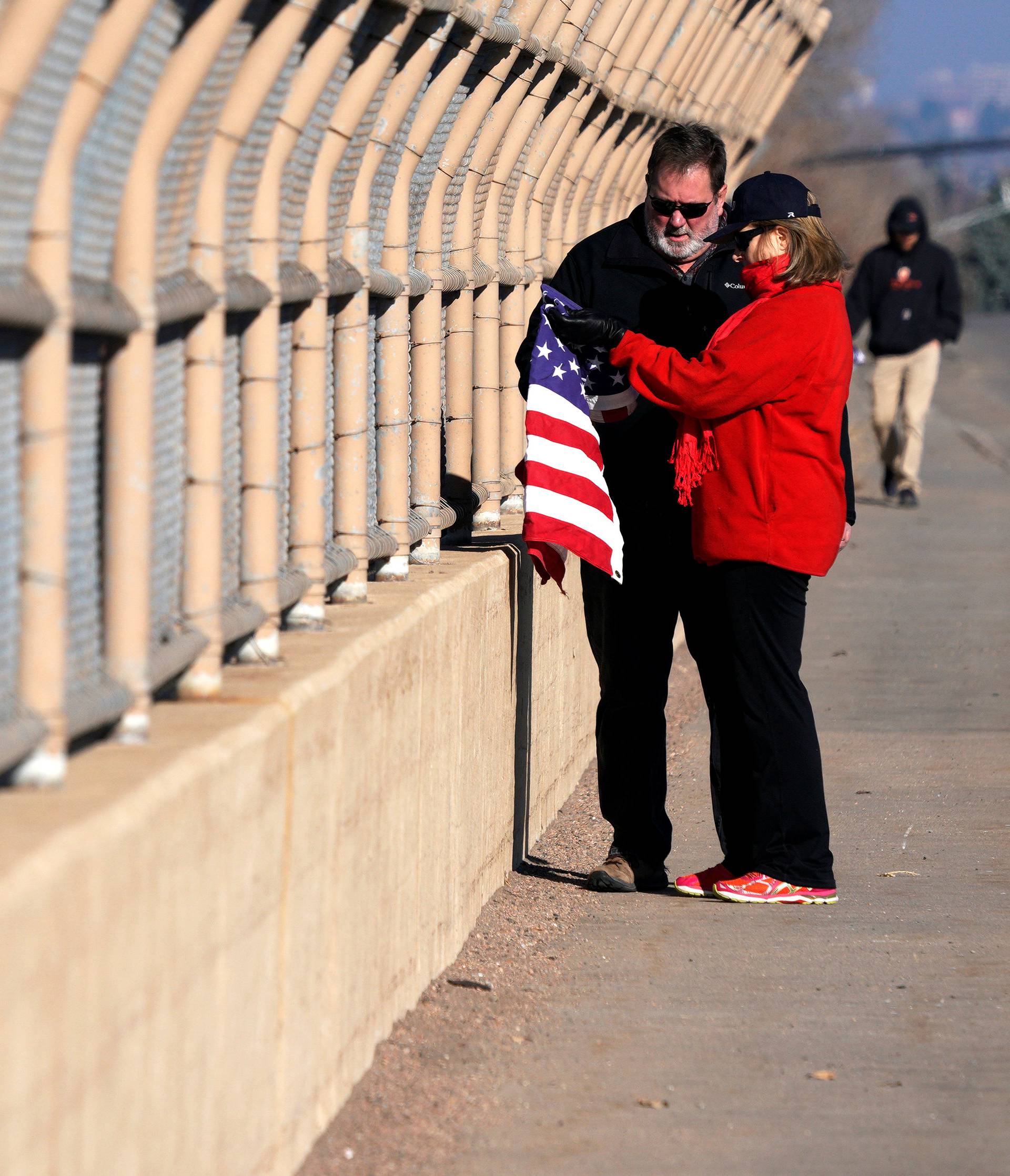 A woman attaches a flag to an overpass where a procession of police vehicles escorted the hearse carrying the body of a deputy killed in a domestic disturbance where multiple deputies and civilians were shot in Highlands Ranch