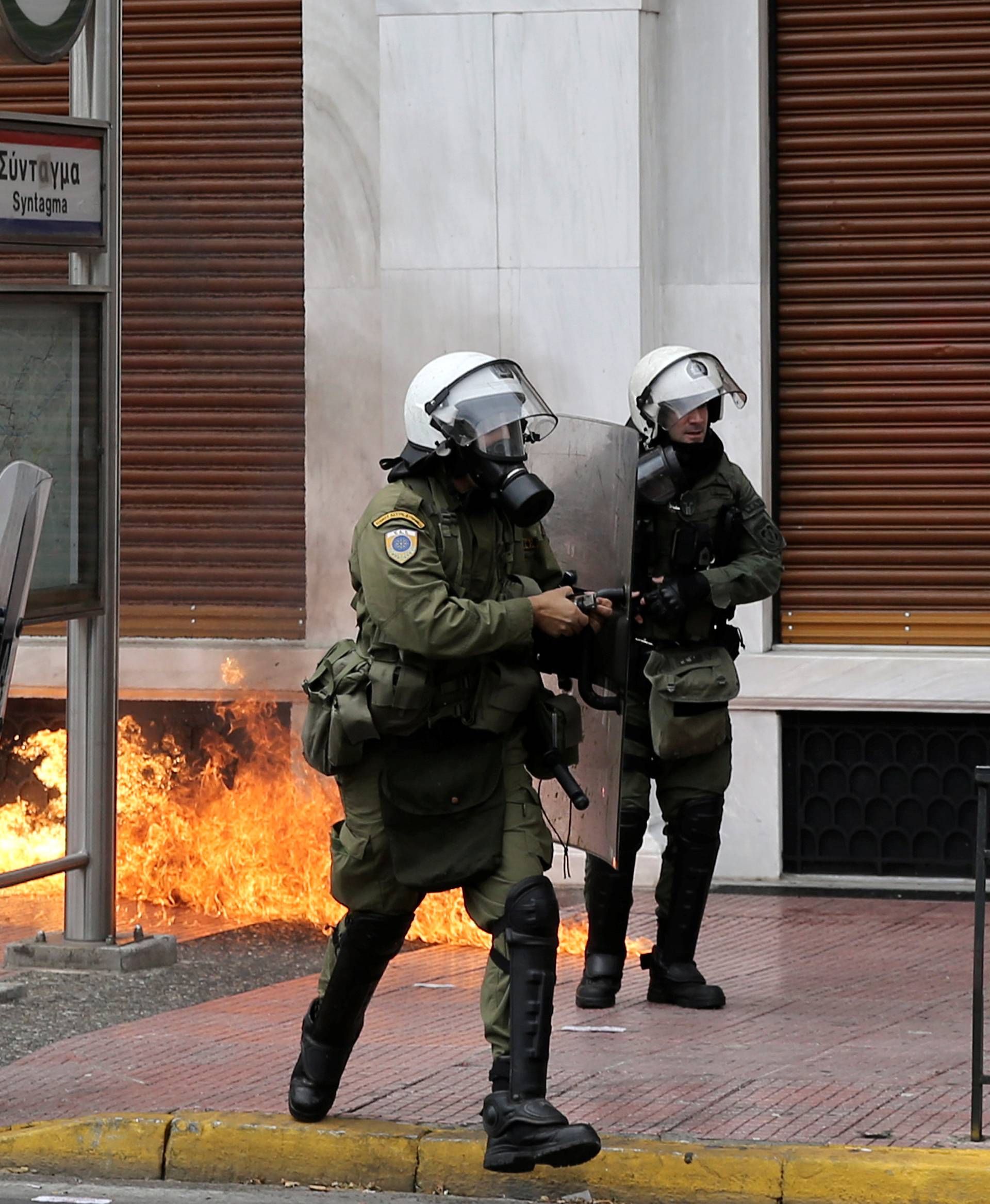 Riot police walk next to flames from a petrol bomb during a 24-hour general strike against the latest round of austerity in Athens