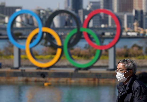 FILE PHOTO: A man walks in front of the Olympic rings at the waterfront area at Odaiba Marine Park in Tokyo