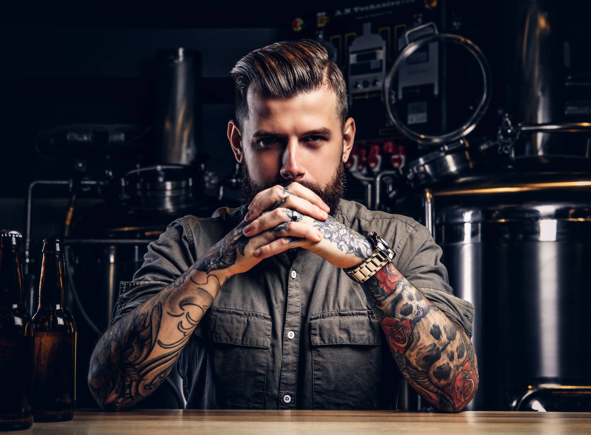 Portrait of a pensive tattooed hipster male with stylish beard and hair in the shirt in indie brewery.