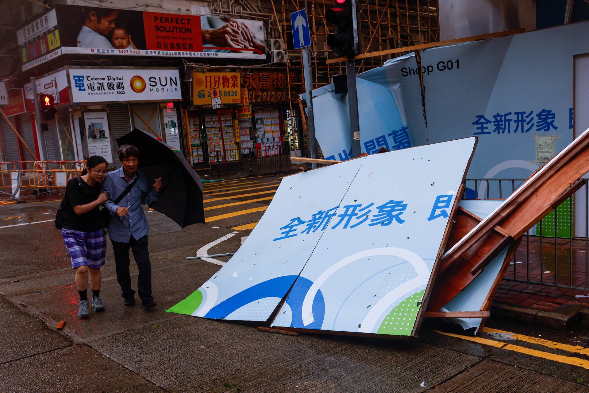 People brave strong winds near a fallen billboard following Super Typhoon Saola, in Hong Kong