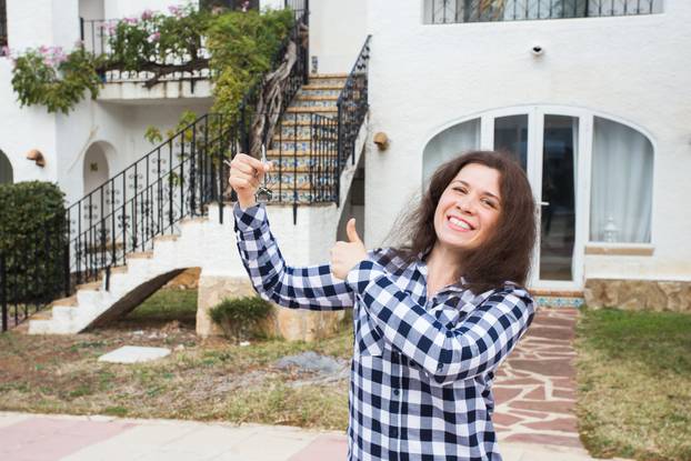 Ownership, real estate, purchase and rent concept - Woman with keys standing outside new home