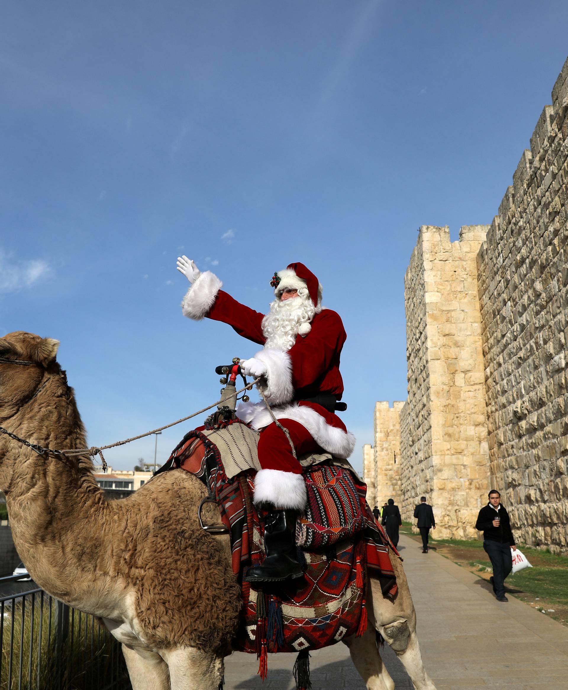 Israeli-Arab Issa Kassissieh rides a camel wearing a Santa Claus costume during the annual Christmas tree distribution by the Jerusalem municipality in Jerusalem's Old City