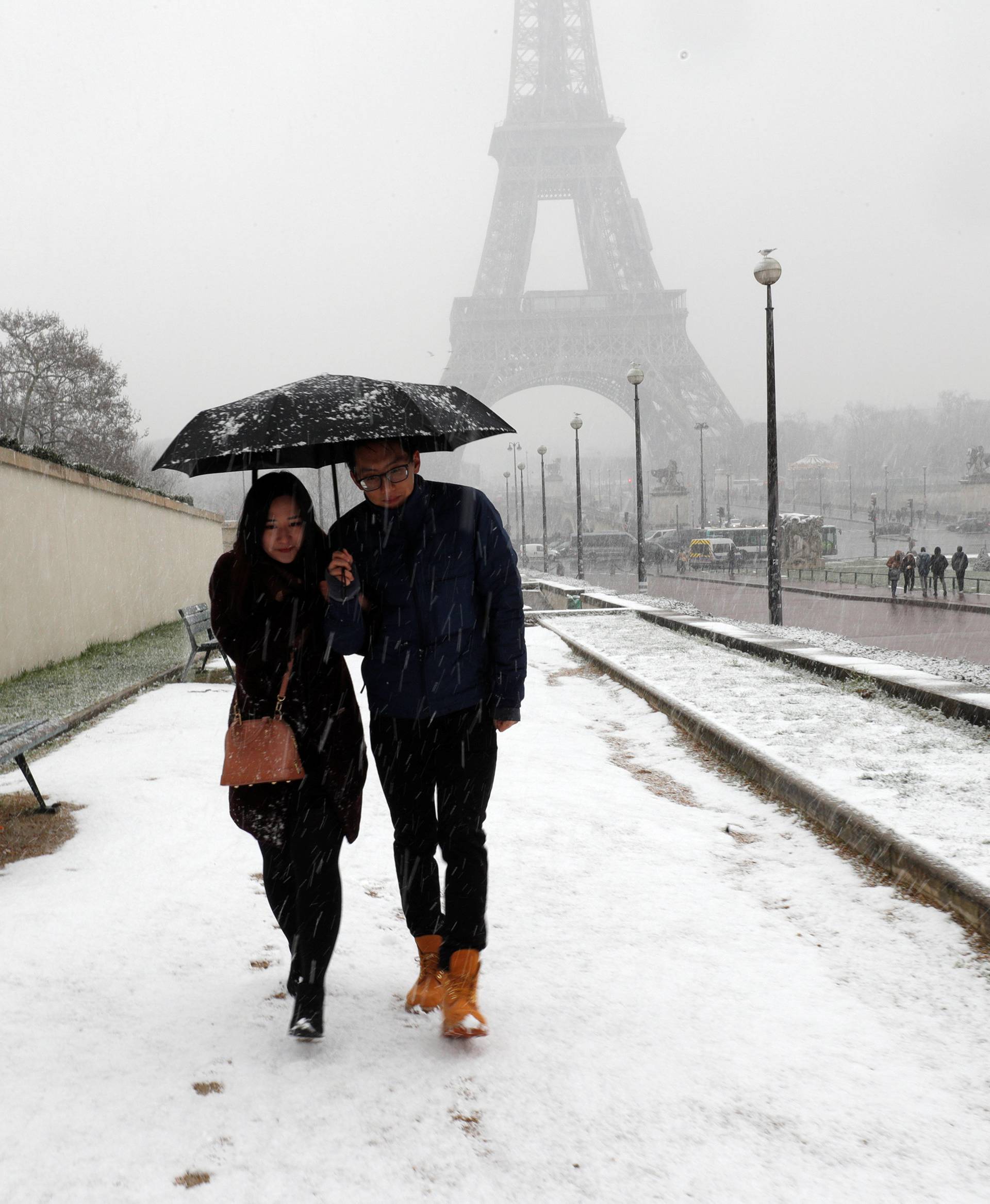 Tourists hold an umbrella as they walk on a snow-covered path towards the Eiffel Tower in Paris, as winter weather with snow and freezing temperatures arrive in France
