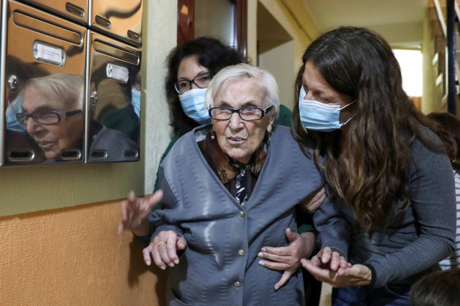 Florentina Martin, a 99 year-old woman who survived coronavirus disease (COVID-19), is helped by her caregiver Olga Arauz and her granddaughter Noelia Valle at the entrance of her home in Pinto
