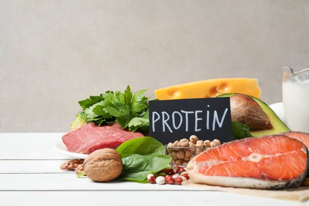 Card with word PROTEIN and different products on white wooden ta