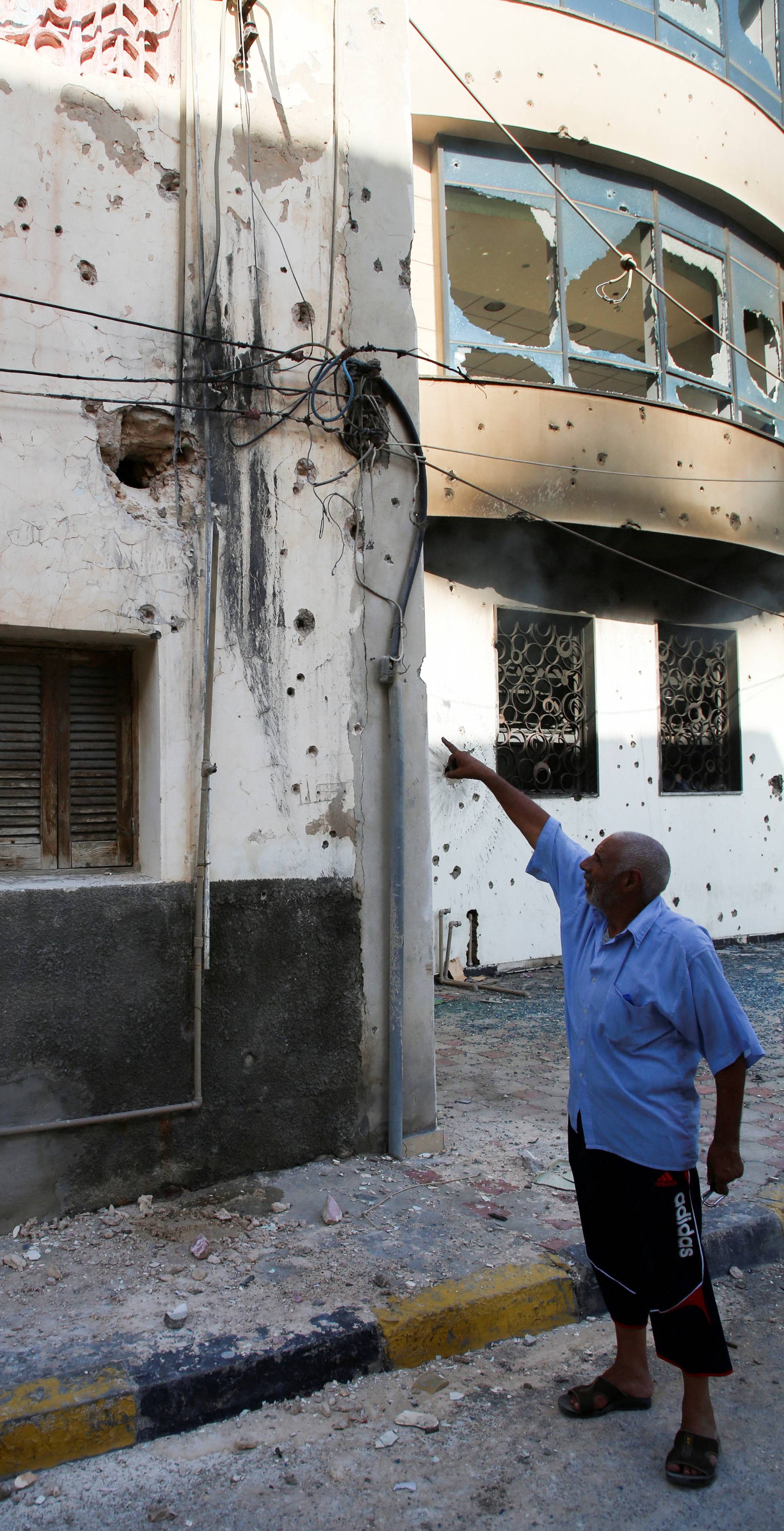A man points at damages on a wall of a house after yesterday's clashes in Tripoli