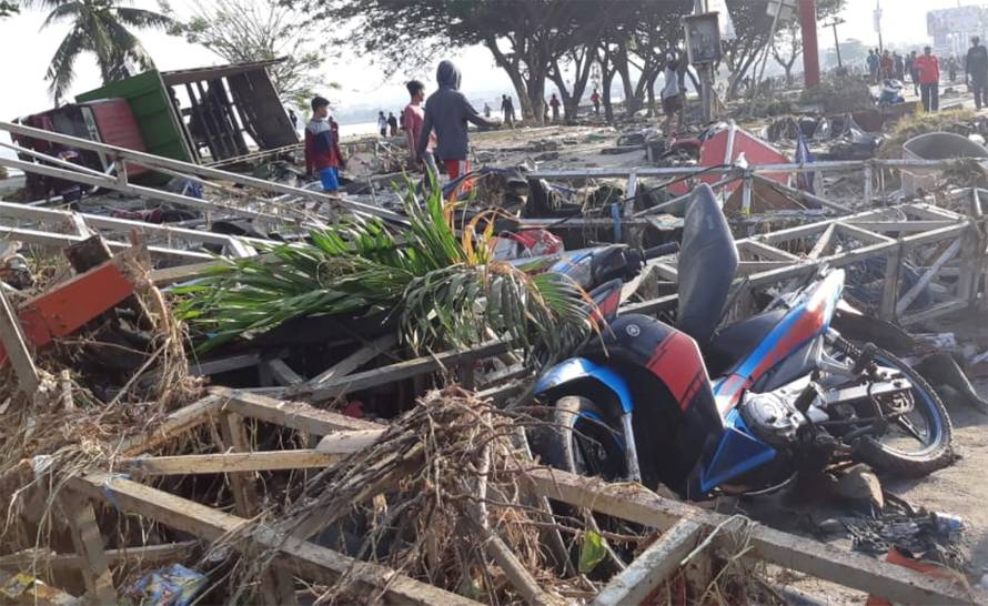 People walk near the ruins of a shop at the beach after a tsunami hit in Palu