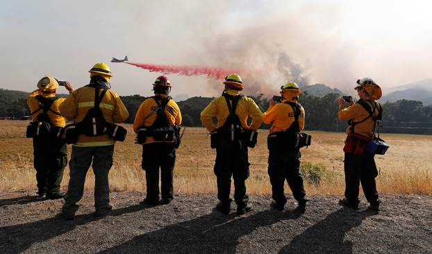 Firefighters watch as an air tanker drops fire retardant along the crest of a hill to protect homes at the  River Fire in Lakeport, California
