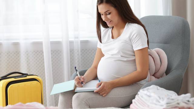 Pregnant woman writing packing list for maternity hospital at ho