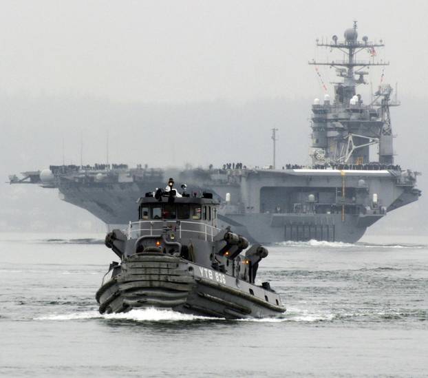 The Nimitz-class aircraft carrier USS Abraham Lincoln (CVN 72) departs Naval Station Everett, Washington, on a scheduled seven-month deployment to the U.S. 5th Fleet area of responsibility, with tugboats assisting in pier operations and ship maneuvering.