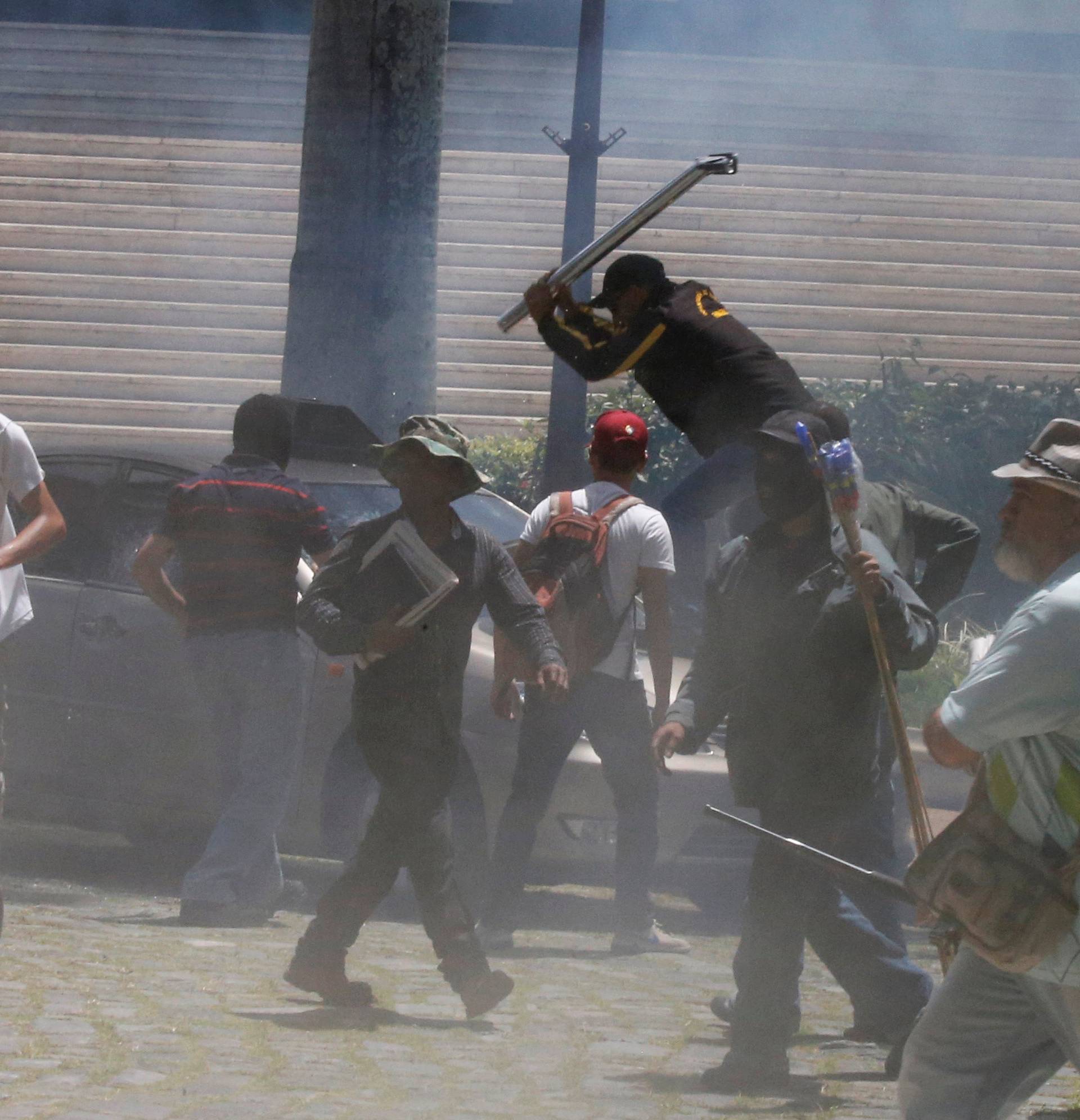 Government supporters break a car outside the National Assembly, in Caracas