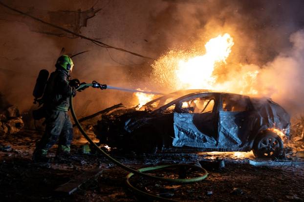 An Israeli firefighter works to put out a fire on a car at the site of a projectile impact, in Tel Aviv
