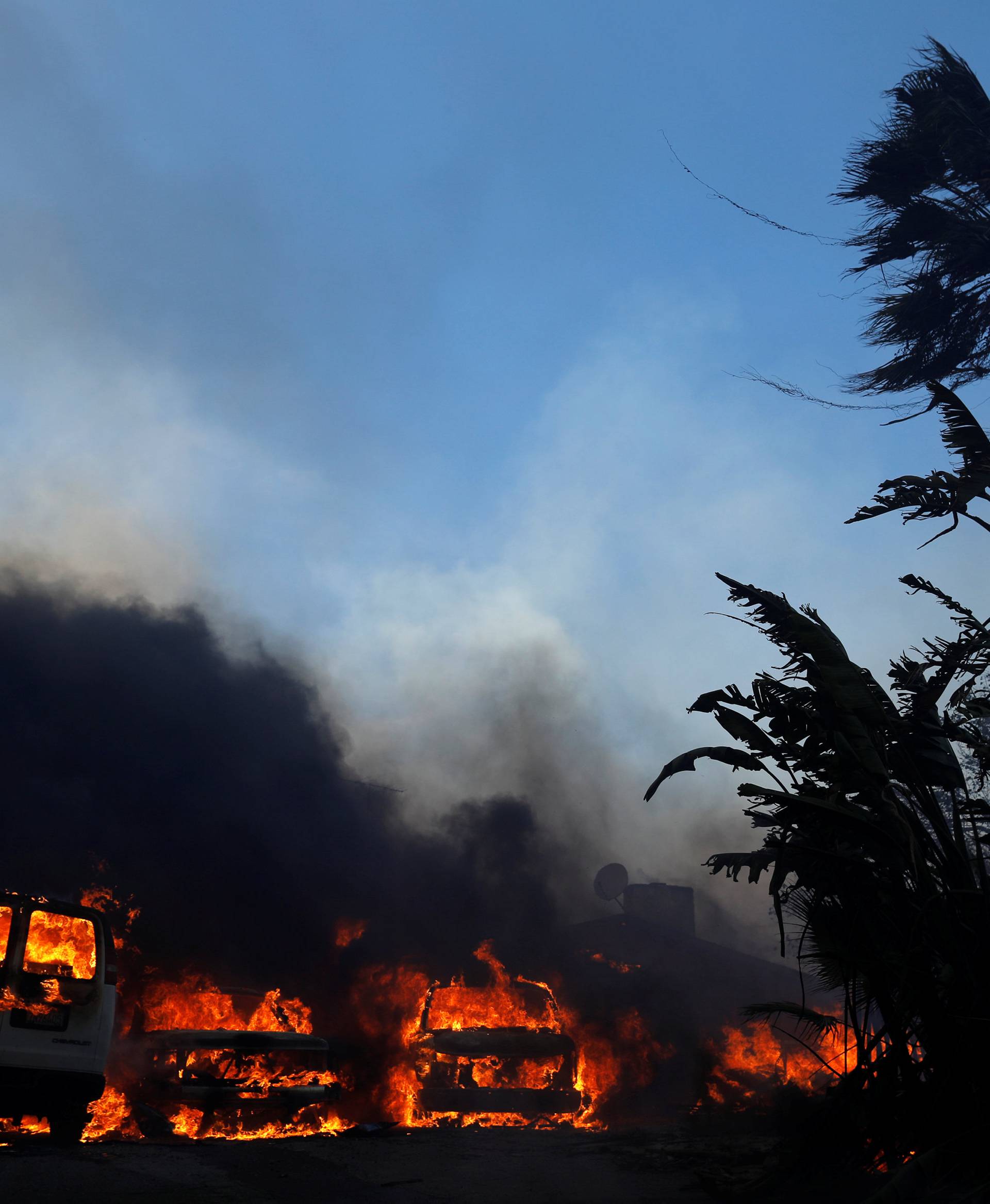 Cars burn along with a home during the Lilac Fire, a fast moving wild fire in Bonsall, California