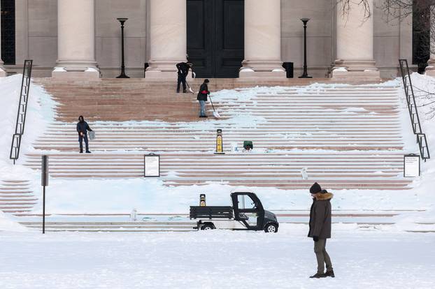 A person walks by workers spreading salt and shoveling the steps of the National Gallery of Art after a winter storm in Washington