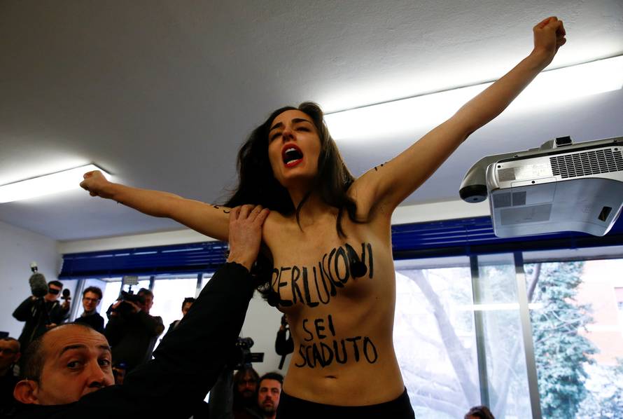 A topless activist of women's rights group Femen interrupts voting as Forza Italia party leader Silvio Berlusconi casts his vote at a polling station in Milan