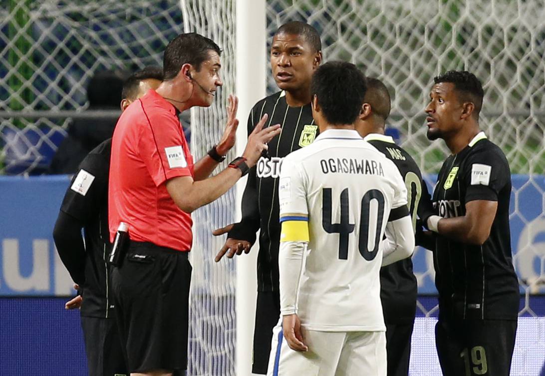 Atletico Nacional players remonstrate with Referee Viktor Kassai as he awards a penalty to Kashima Antlers