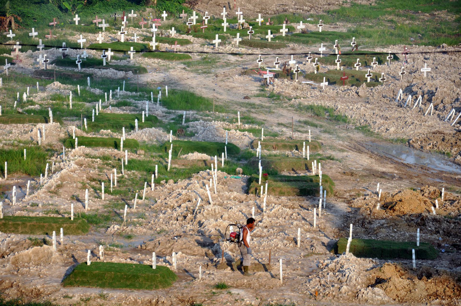 Worker walks through grave site provided by government for COVID-19 victims in Medan